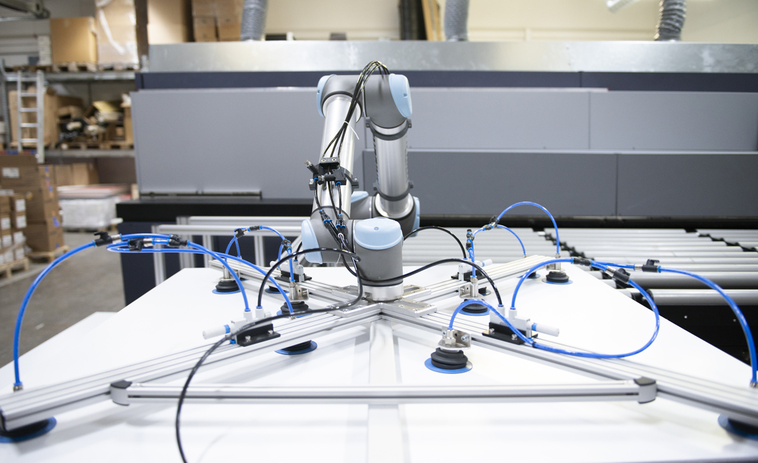 Industriel robotarm på en hvid platform med blå pneumatiske rør til automatisering.