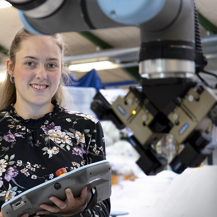 Kvinde i industrien styrer robotarm med kontrolpanel.